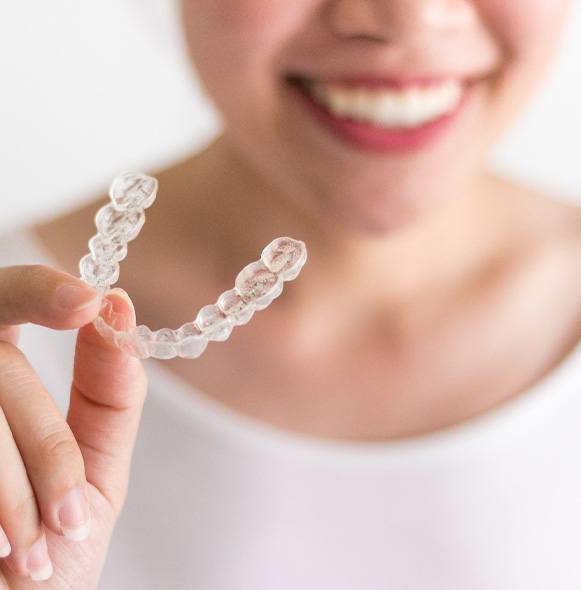 Woman in white smiling holding Invisalign