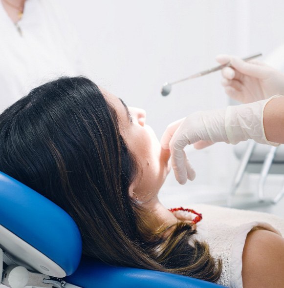 Dentist in white gloves holding mirror and touching patient’s mouth
