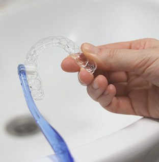 Hands brushing clear aligner at sink