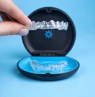 Two fingers lifting Invisalign from its tray