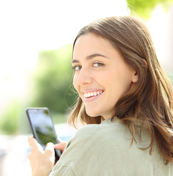 Woman with beautiful smile texting on phone outside