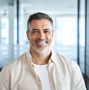 Senior man standing and smiling in room with glass walls