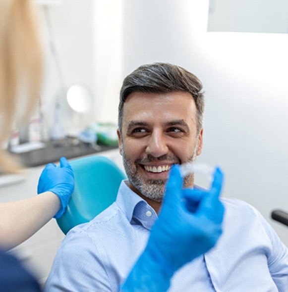 Smiling man looking at dental assistant holding clear aligner