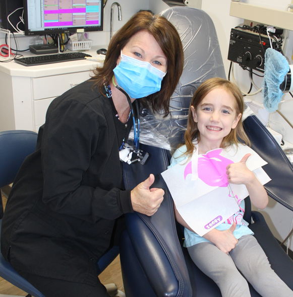 Dental team member and young patient giving thumbs after dental sealant placement
