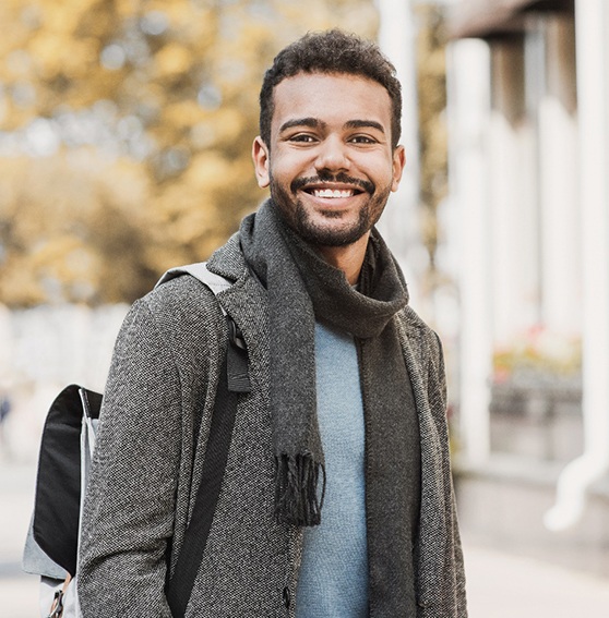 Man walking outside smiling and wearing a scarf