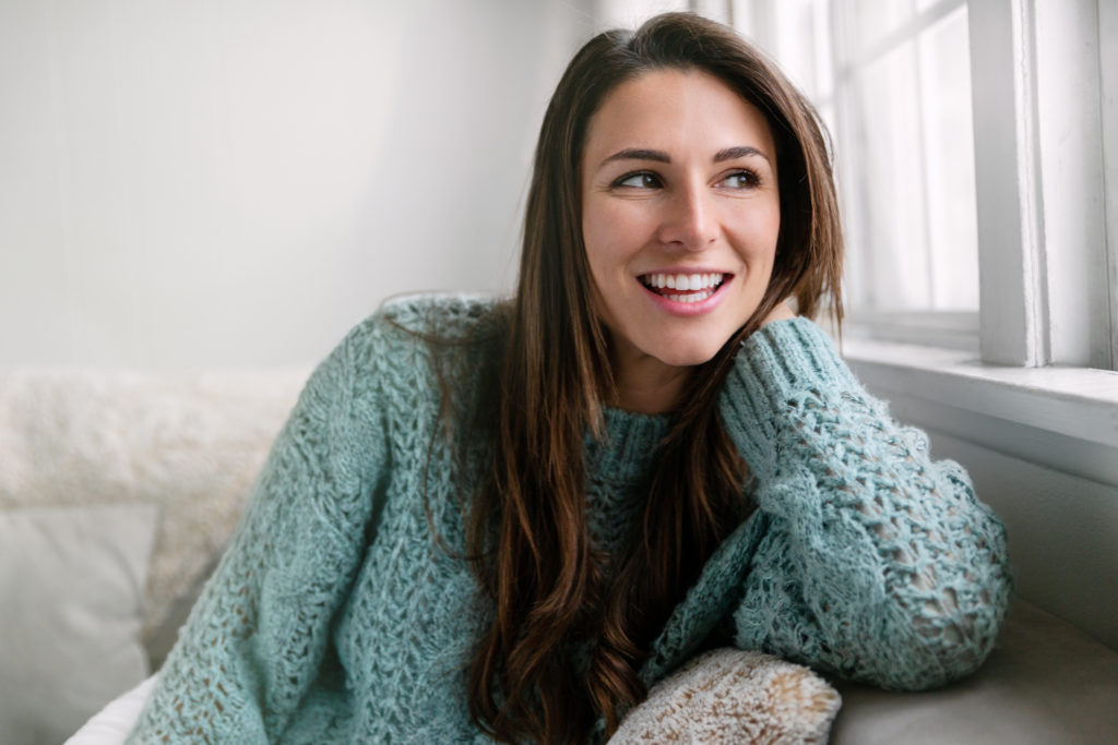 Woman with straight teeth leaning on couch and smiling