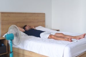 Man resting on bed in front of fan
