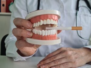 Hand holding set of artificial teeth that are biting a cigarette