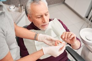 Dentist handing dentures to man in dental chair